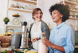 Two women in a kitchen, one operating a blender while the other observes, surrounded by fresh ingredients Two women in a kitchen, one operating a blender while the other observes, surrounded by fresh ingredients